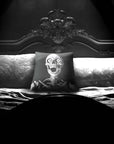 Skeleton Peekaboo pillow by Muahaha!  Black and white photo of the 16x16 faux suede pillow showing a skeleton's face resting on an antique bed in a victorian mansion.  The perfect gothic, horror gift!